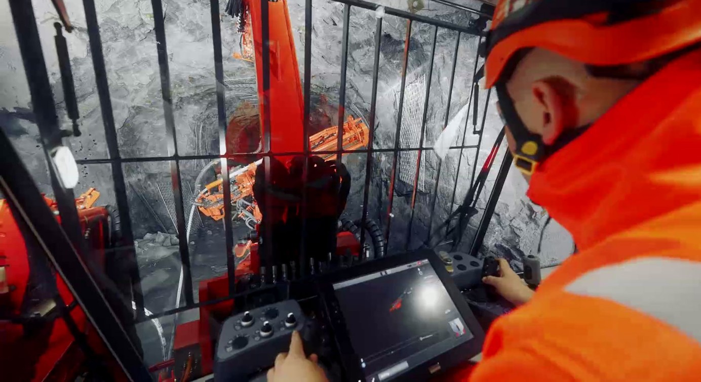 An underground operator in safety clothing navigating a drill boom by using the drill's digital interface in a cabin in an underground tunnel