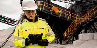 A woman in work clothes and helmet standing in front of a screening station at a quarry