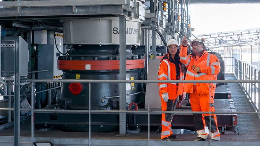 A woman and a man wearing personal protective equipment in a rock processing facility.