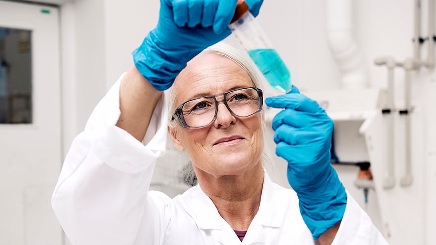 A woman wearing blue plastic gloves holding a test tube